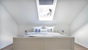 Una camera da letto con un lucernario, un letto con biancheria bianca e un comodino con una lampada.
