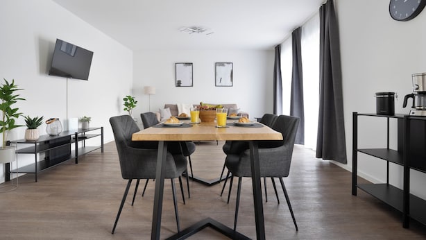 Zona pranzo moderna con tavolo rettangolare, quattro sedie, televisore a schermo piatto montato a parete e macchina del caffè su uno scaffale.