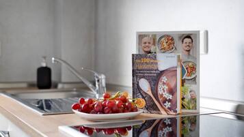 Un plan de travail de cuisine avec une assiette de raisins rouges, un robinet en acier inoxydable et un livre de cuisine intitulé « Les 100 meilleurs produits ménagers » sur une étagère.