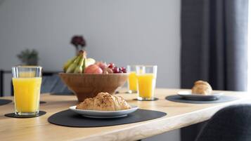 Aamiaispöydällä on croissantteja, hedelmäkulho ja lasit täynnä appelsiinimehua.