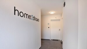 Un corridoio con un cartello 'home2share' appeso al muro, una porta bianca in fondo e un pavimento piastrellato.