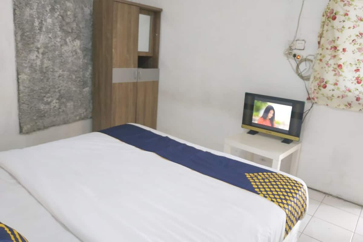 Ein Schlafzimmer mit einem Bett, einem Holzschrank, einem Fernseher auf einem kleinen Tisch und einem blumigen Vorhang.