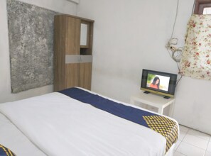 A bedroom with a bed, a wooden wardrobe, a television on a small table, and a floral curtain. - SPOT ON 93016 Griya Kamboja Cijantung  (Jakarta)