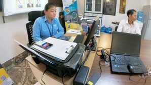 An office with two people working at desks with laptops, a whiteboard with travel-related images, and a banner for Sarah Transport Co. Ltd. - Sarah Guest House (Siem Reap)