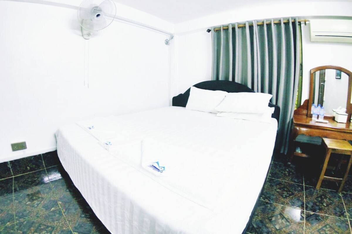 Habitación de hotel con cama, escritorio, silla, espejo, cortina y unidad de aire acondicionado.
