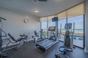 Ein Fitnessstudio mit Laufbändern, Kraftgeräten und einem großen Fenster mit Blick auf einen Strand.