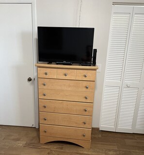 A wooden dresser with a flat-screen TV on top, located in a room with wooden flooring and white walls. - Oceanfront Condo on traffic free beach - Great views from 403 Lighthouse Shores (Ponce Inlet)