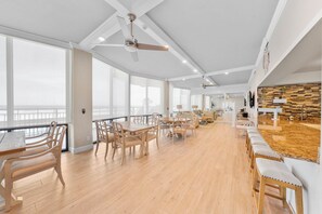 Uma sala de jantar espaçosa com soalho de madeira, grandes janelas e vista para o mar.
