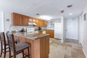 A kitchen with wooden cabinets, a granite countertop, a built-in stove, and a refrigerator. - Oceanfront Condo on traffic free beach - Great views from 403 Lighthouse Shores (Ponce Inlet)