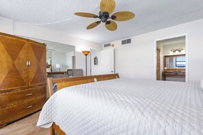 Quarto de hotel com uma cama grande, um guarda-roupa, um ventilador de teto e um banheiro visível por uma porta aberta.