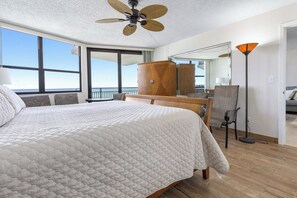 Ein Hotelzimmer mit einem großen Bett, einem Deckenventilator, einem Schreibtisch, einem Sessel und Meerblick.