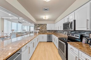 A modern kitchen with white cabinets, granite countertops, a built-in oven, microwave, and dishwasher. - Oceanfront Condo on traffic free beach - Great views from 403 Lighthouse Shores (Ponce Inlet)