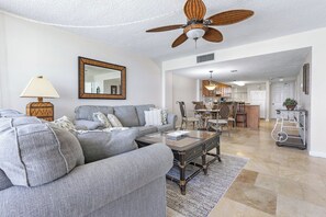 A modern living room with a sofa, coffee table, and a dining area in the background. - #403 Lighthouse Shores 2/2  Oceanfront Condo Traffic Free Beach (Ponce Inlet)