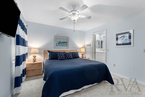 Une chambre à coucher avec un lit, des tables de chevet, un ventilateur de plafond et un tableau accroché au mur.