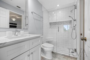 Une salle de bain moderne avec une douche à parois de verre, des carreaux blancs, un sol en marbre et un grand miroir au-dessus du lavabo.