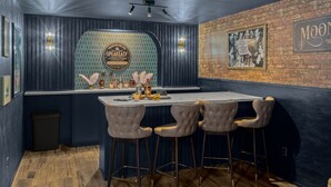 Angolo bar con parete blu scuro, parete decorativa in mattoni e bancone bar bianco. Sono presenti quattro sgabelli da bar e un quadro incorniciato sulla parete in mattoni.