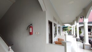 A covered corridor with a fire extinguisher mounted on the wall, a staircase, and a series of doors leading to rooms. - OYO 93051 Wisma Syariah Buloe Near Lapangan Abubakar Lambogo Batili Enrekang (Enrekang)