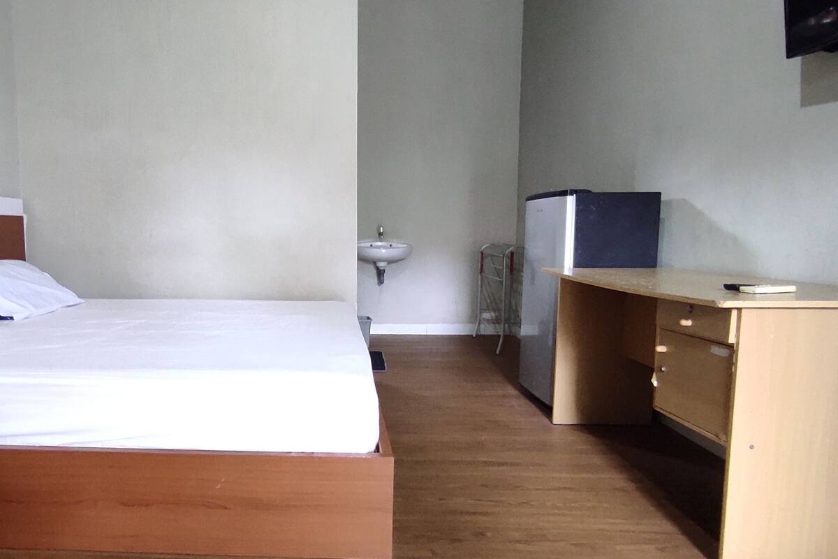 Een slaapkamer met een houten bed, een nachtkastje, een klein bureau en een aan de muur bevestigde televisie.