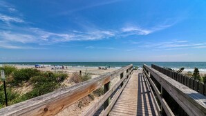 Une promenade en bois menant à une plage où se trouvent des gens et des parasols.