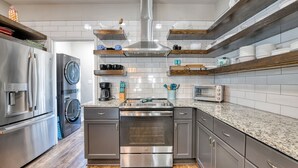 Une cuisine moderne dotée d’appareils électroménagers en acier inoxydable, d’étagères en bois et d’un revêtement mural en carreaux.