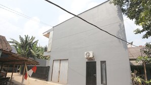 A modern two-story building with a grey exterior, a black door, and an air conditioning unit mounted on the wall. - OYO 93021 Kost Dison (Bekasi)