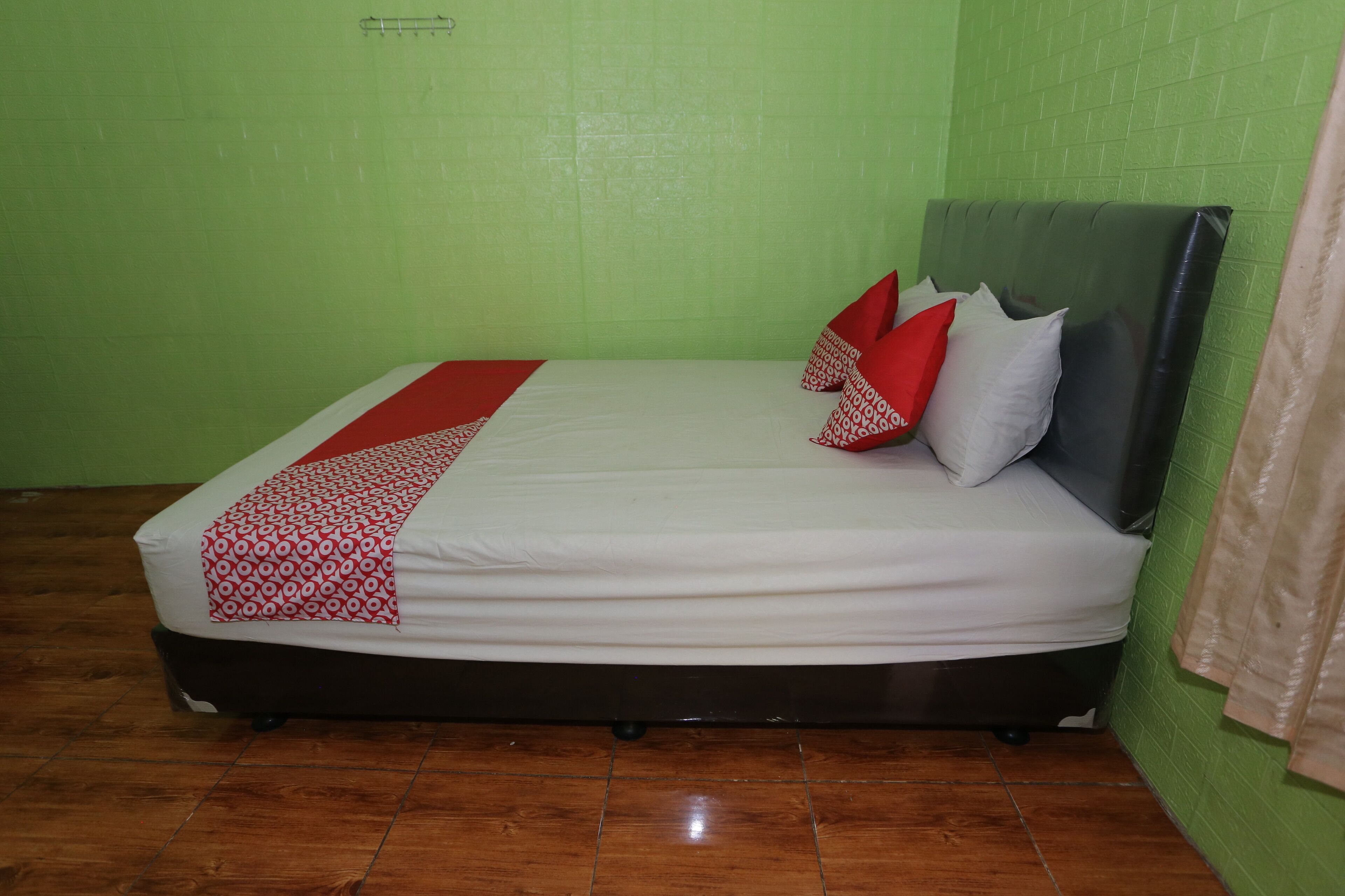 Un lit avec un matelas blanc, une couvre-lit à motifs rouges et blancs, et plusieurs oreillers, dans une pièce aux murs verts et au plancher en bois.