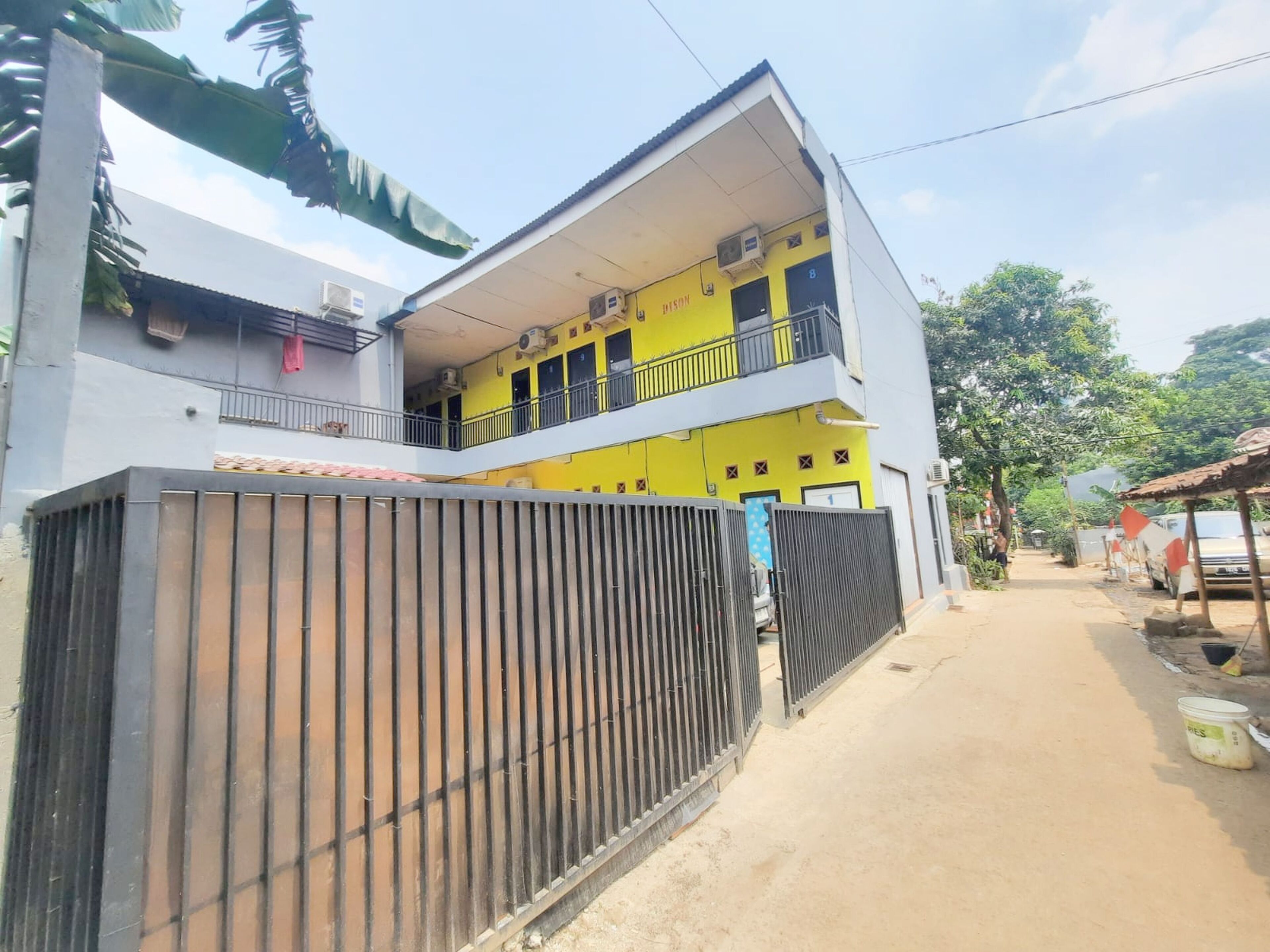 A two-story building with a yellow facade, a balcony on the upper floor, and a gated entrance.
