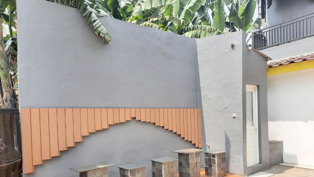 A modern outdoor seating area with stone tables and a grey wall with a wooden panel design. - OYO 93021 Kost Dison (Bekasi)