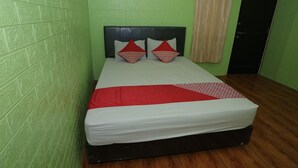 A single bed with a black headboard, a red and white bedspread, and two red pillows. The room has green walls and a wooden floor. - OYO 93021 Kost Dison (Bekasi)