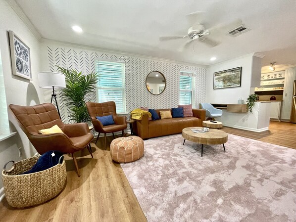 A modern living room with a brown leather sofa, two armchairs, a round coffee table, and a large potted plant.