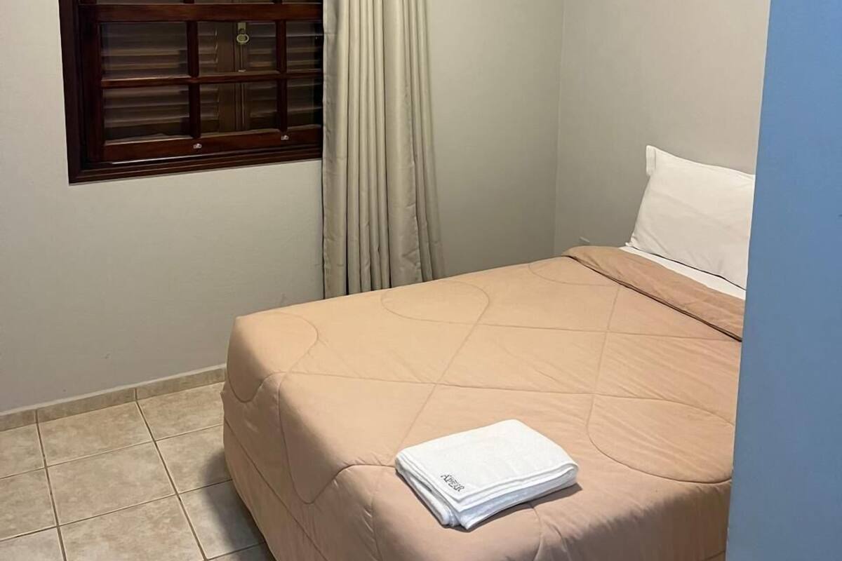 A bedroom with a bed, a window with curtains, and a tiled floor.