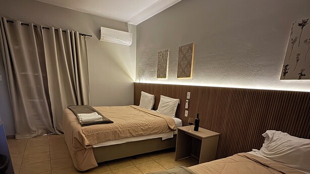 A hotel room with two beds, a bedside table with a wine glass, a wall-mounted air conditioner, and a curtain. - Pousada Apear (Andradas)