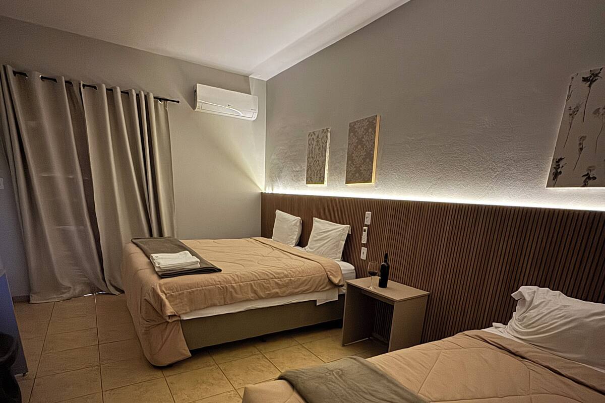 A hotel room with two beds, a bedside table with a wine glass, a wall-mounted air conditioner, and a curtain.