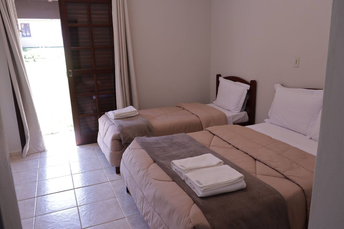 A hotel room with two beds, each with a brown bedspread and white pillows. There is a small table with folded white towels in front of the beds.