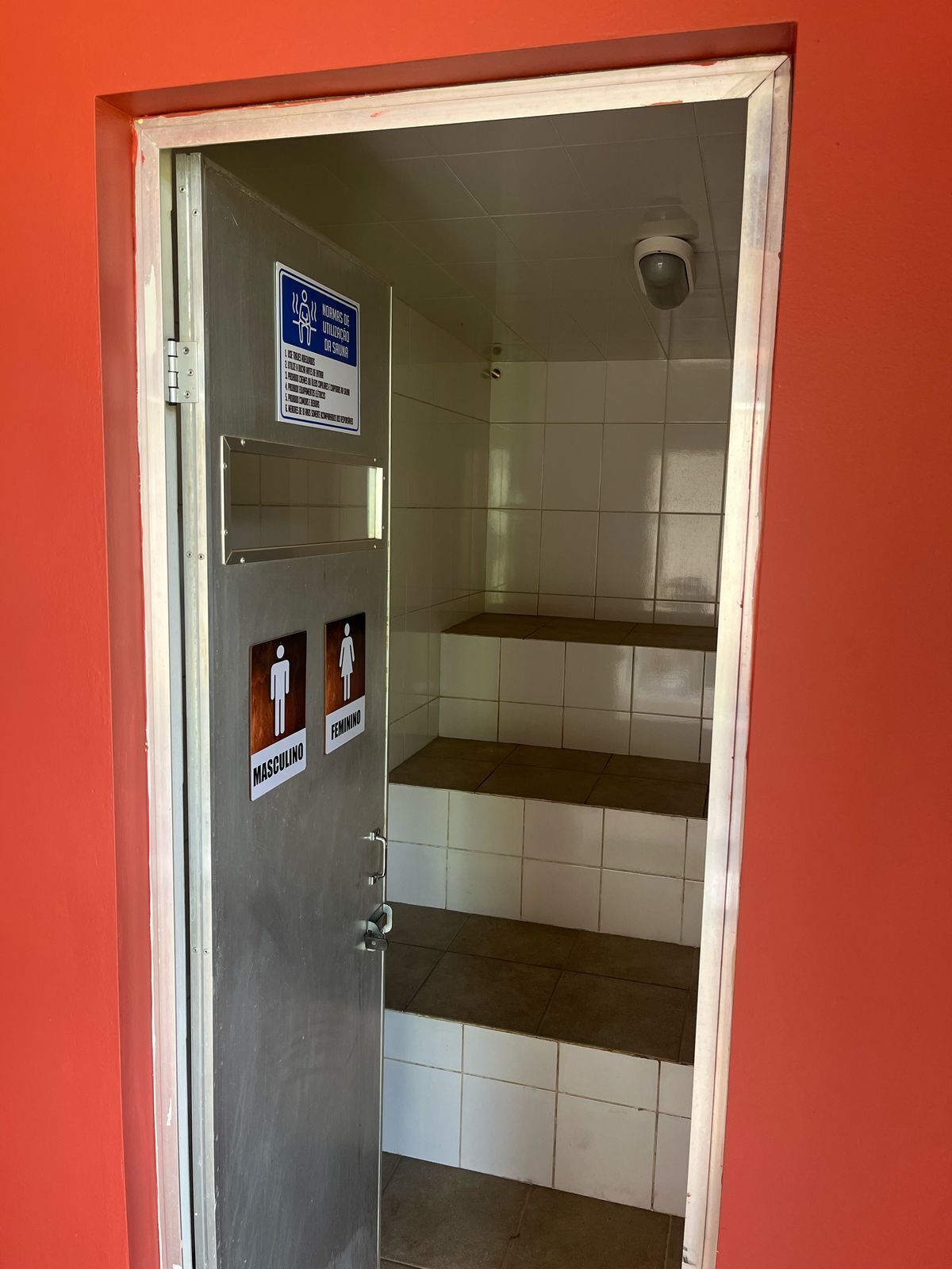 Um banheiro com sinalização indicando instalações separadas para homens e mulheres, e piso cerâmico.