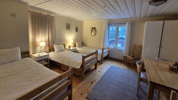 A room with two wooden beds, a wooden table, a chair, a window with curtains, and a radiator.