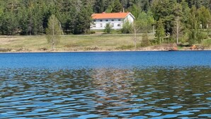 Een huis aan een meer, met een bos op de achtergrond.