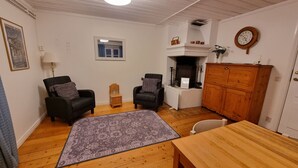 Een gezellige kamer met twee fauteuils, een klein houten kastje, een tafel en een open haard.