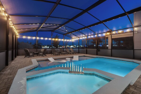 A covered outdoor swimming pool with lounge chairs and string lights.