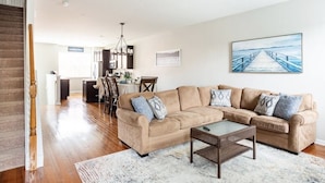 A spacious living room with a beige sectional sofa, a glass coffee table, and a dining area with a table and chairs.