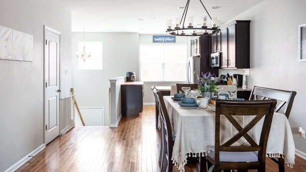 A modern kitchen with dark cabinets, a chandelier, and a dining area with a table set for four.