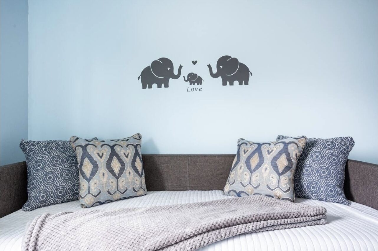 A bedroom with a bed, patterned pillows, and a wall decal of elephants with a heart.