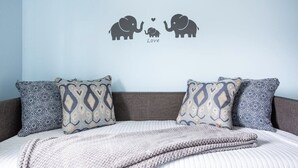 A bedroom with a bed, patterned pillows, and a wall decal of elephants with a heart.