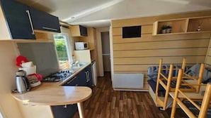 A compact kitchen with a stove, sink, and microwave. There is a small dining area with a table and chairs. - Modern Mobilome (Petit-Caux)