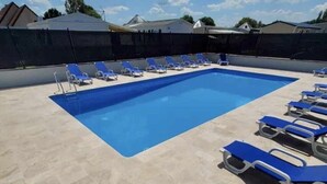 A rectangular swimming pool with blue water, surrounded by a tiled deck. There are multiple blue lounge chairs arranged around the pool. - Modern Mobilome (Petit-Caux)