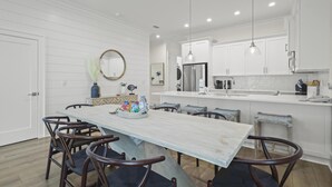 A modern kitchen with white cabinetry, a stainless steel refrigerator, and a dining area with a wooden table and chairs.