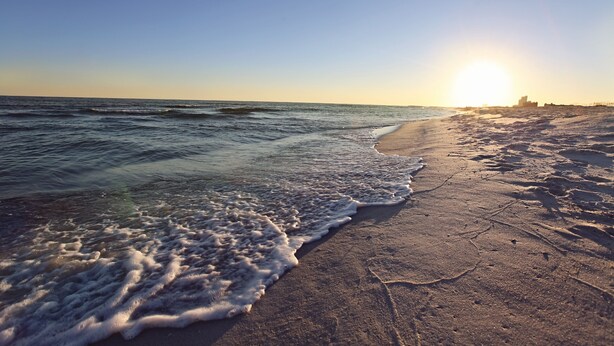 A beach with waves, a clear sky, and the sun setting or rising.