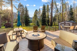 Eine Terrasse mit Gartenmöbeln, einem Feuerkorb und einem kleinen Schuppen in bewaldeter Landschaft.