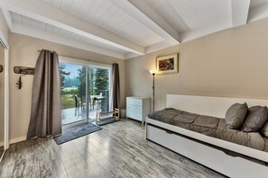 A bedroom with a bed, a desk, a chair, and a view of the outdoors.