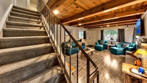 Una escalera con peldaños alfombrados y barandillas de metal que conduce a una sala de estar con piso de madera, sofás de cuero verde y una chimenea.